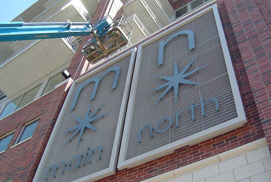 Custom fabricated water jet cut exterior sign is hoisted by crane into place at Main North Loft's