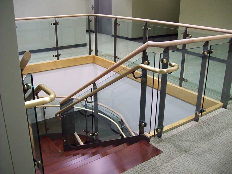Ornamental custom metal railings at balcony fabricated using tempered glass panels, brass sub-rails and wood cap rail.